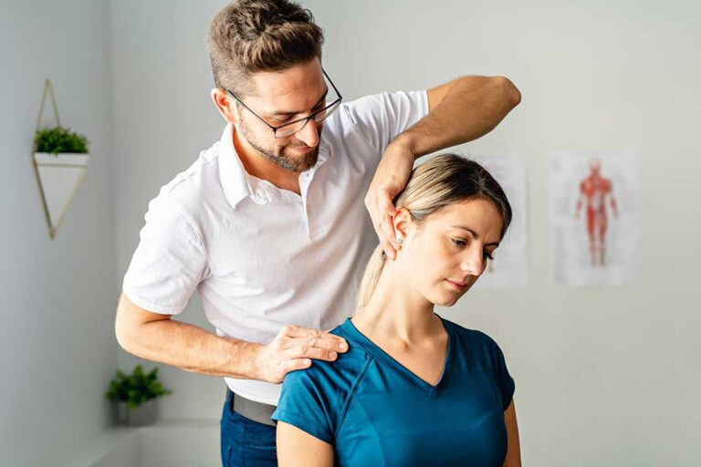 Woman with hands on lower back, standing in a home bedroom, expressing mild discomfort.
